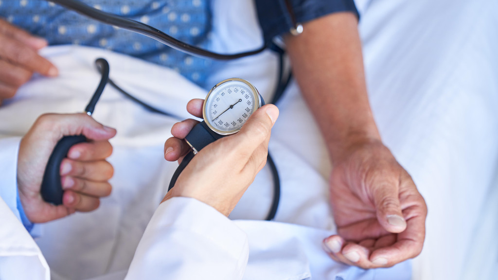Hand von Arzt hält Blutdruckmessgerät beim Blutdruck messen bei einem Patienten