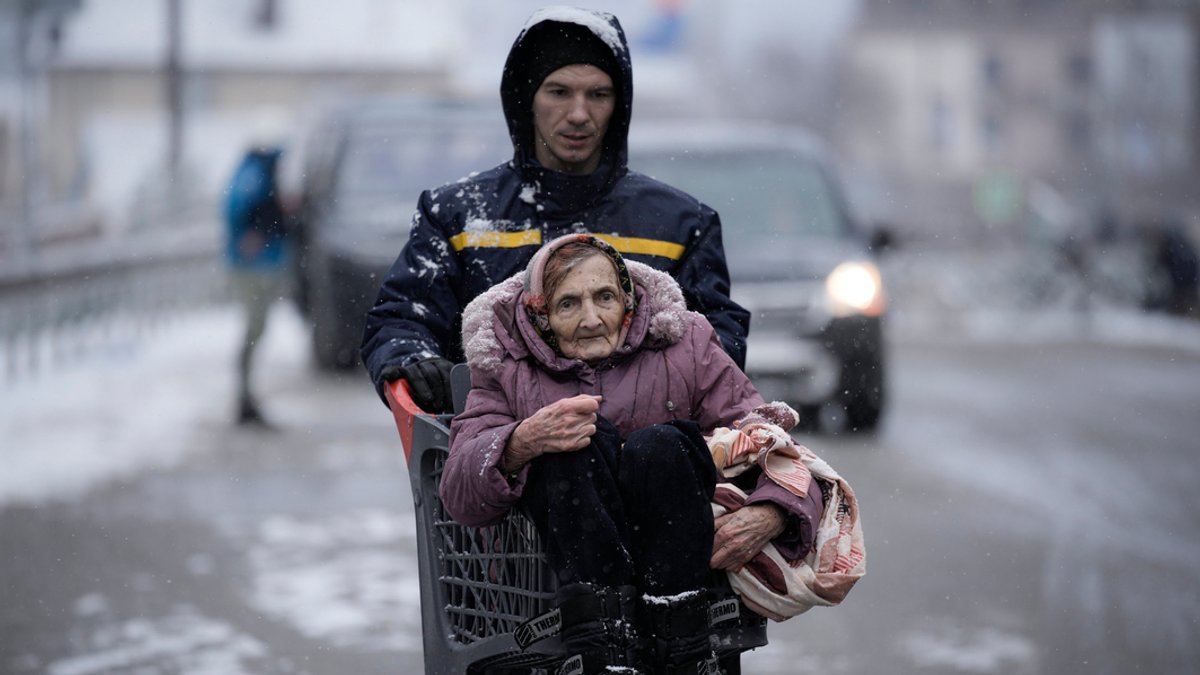 Ukraine, Irpin: Ein Mann transportiert nach Evakuierungsmaßnahmen in Irpin eine ältere Frau in einem Einkaufswagen.
