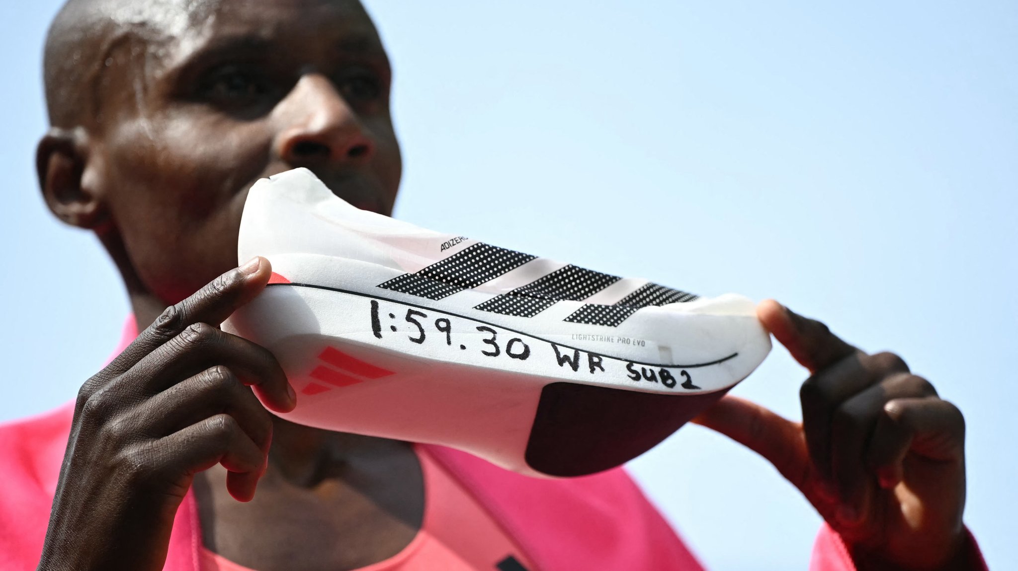 Ein Mann hält einen Schuh hoch, auf dem steht: "1:59:30 WR SUB2"