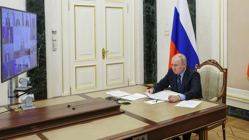 Der russische Präsident an einem Tisch mit einem Bildschirm, auf dem Gesprächsteilnehmer zu sehen sind