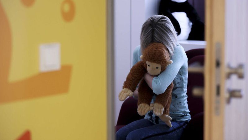 Eine junge Frau sitzt mit einem Kuscheltier im Arm in einem Raum, in dem Kinder und Jugendliche, die von Missbrauch betroffen sind, vernommen werden können. | Bild: dpa-Bildfunk/Jan Woitas Eine junge Frau sitzt mit einem Kuscheltier im Arm in einem Raum, in dem Kinder und Jugendliche, die von Missbrauch betroffen sind, vernommen werden können.