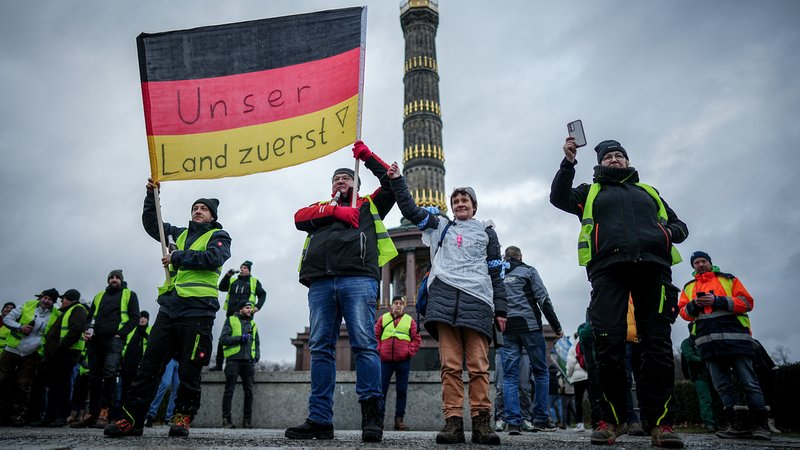 Menschen protestieren mit einer Deutschlandfahne mit der Aufschrift "Unser Land zuerst" vor der Siegessäule in Berlin.
