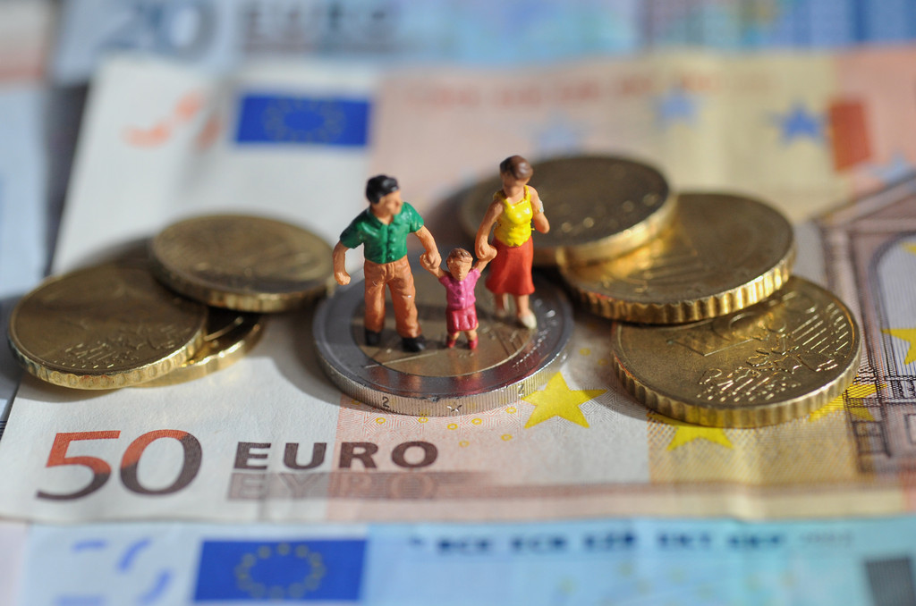 Eine Familie aus Spielzeugfiguren steht auf einem 50-Euro-Schein, darum ist Kleingeld angeordnet.