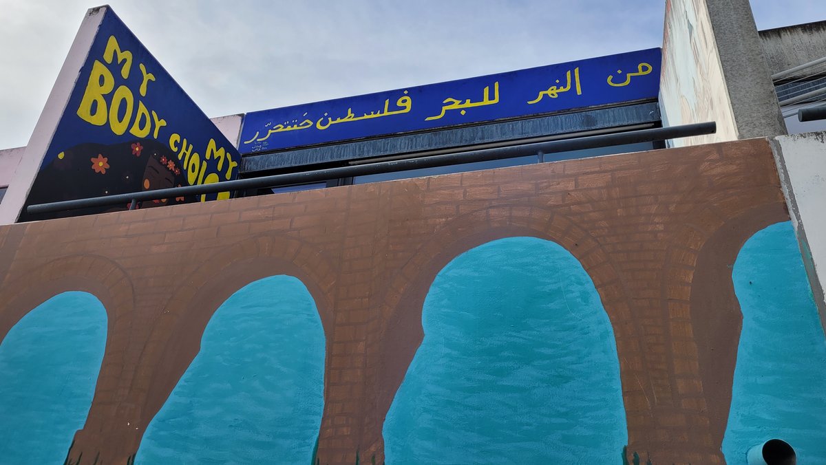 "Vom Fluss bis zum Meer wird Palästina frei sein" steht in Arabisch auf blauem Untergrund auf einem Bungalow im Olympiadorf in München.