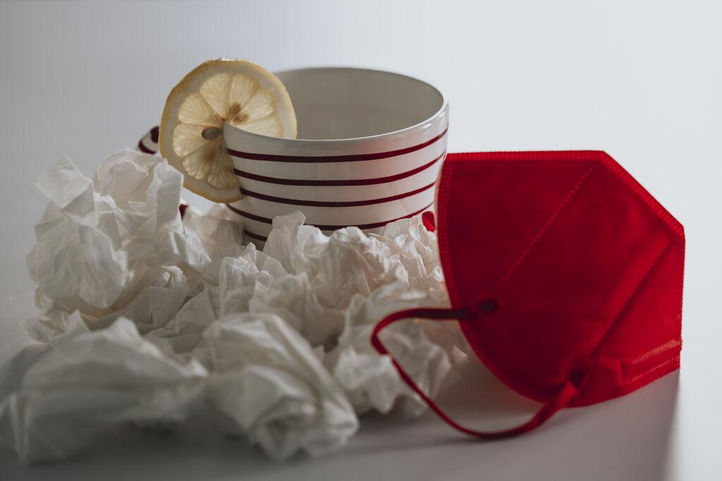 Tasse mit einer Scheibe Zitrone, gebrauchte Taschentücher und eine rote FFP2-Maske (Symbolbild)