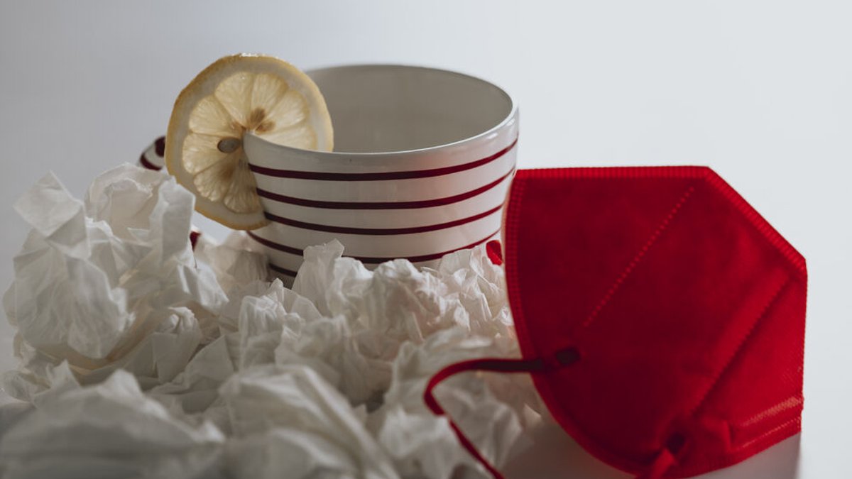 Tasse mit einer Scheibe Zitrone, gebrauchte Taschentücher und eine rote FFP2-Maske (Symbolbild)