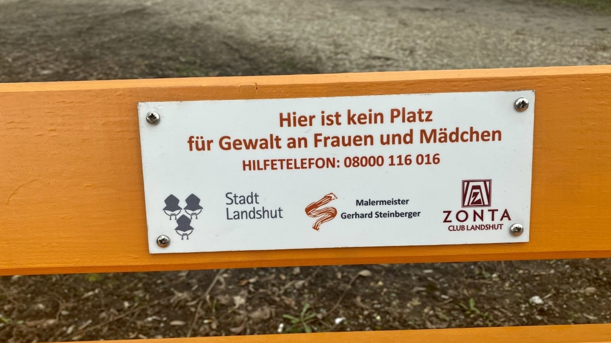 Eine weiße Plakette auf der orangen Bank