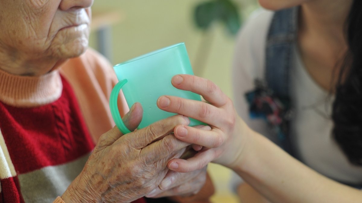 Eine Pflegekraft hilft einer alten Frau beim Trinken aus einem Becher