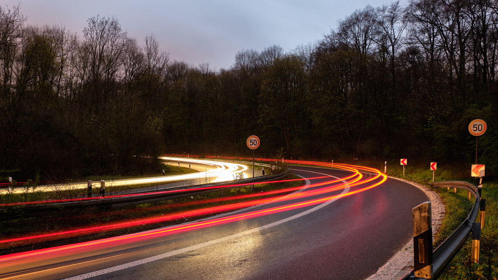 Lichtspur auf einer Straße mit Tempo 50 Schildern in einer steilen Kurve
