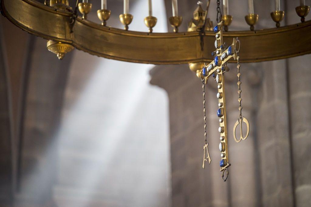 Ein Kreuz  aus Messing steht im Bamberger Dom, im Hintergrund scheint die Sonne durch ein Kirchenfenster.