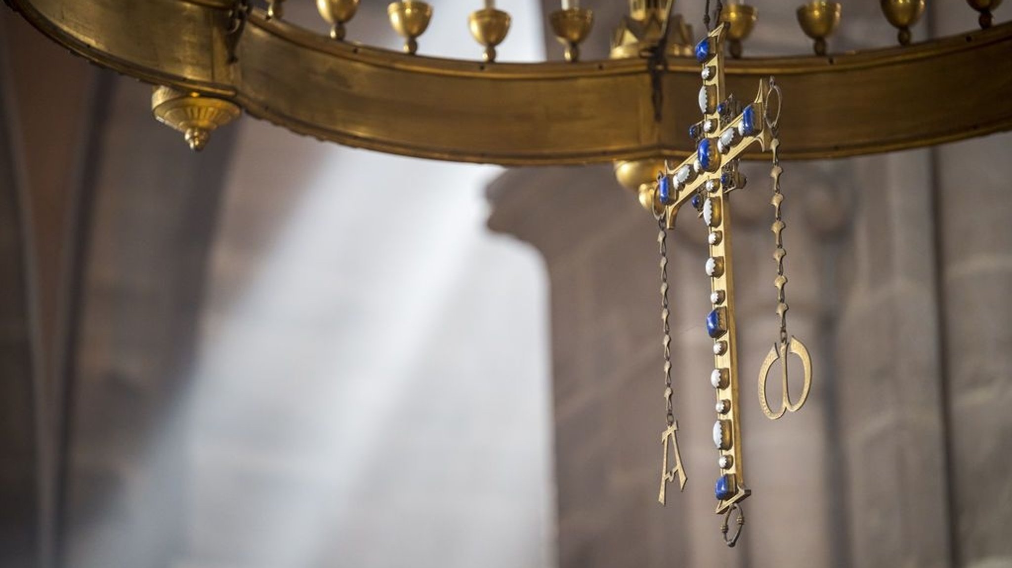 Ein Kreuz  aus Messing steht im Bamberger Dom, im Hintergrund scheint die Sonne durch ein Kirchenfenster.