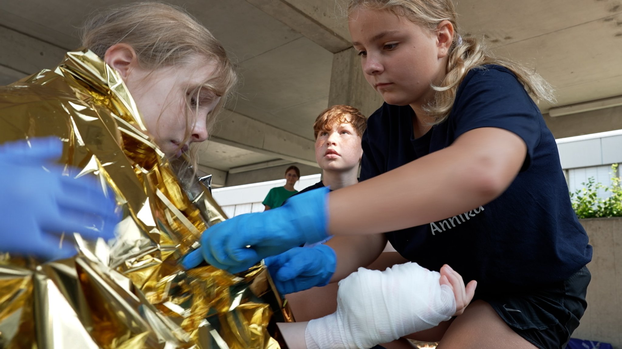 In einem gespielten Szenario legt eine junge Ersthelferin eine Wärmedecke über die Schultern einer verletzten Person. | Bild: BR/Simon Frick In einem gespielten Szenario legt eine junge Ersthelferin eine Wärmedecke über die Schultern einer verletzten Person.
