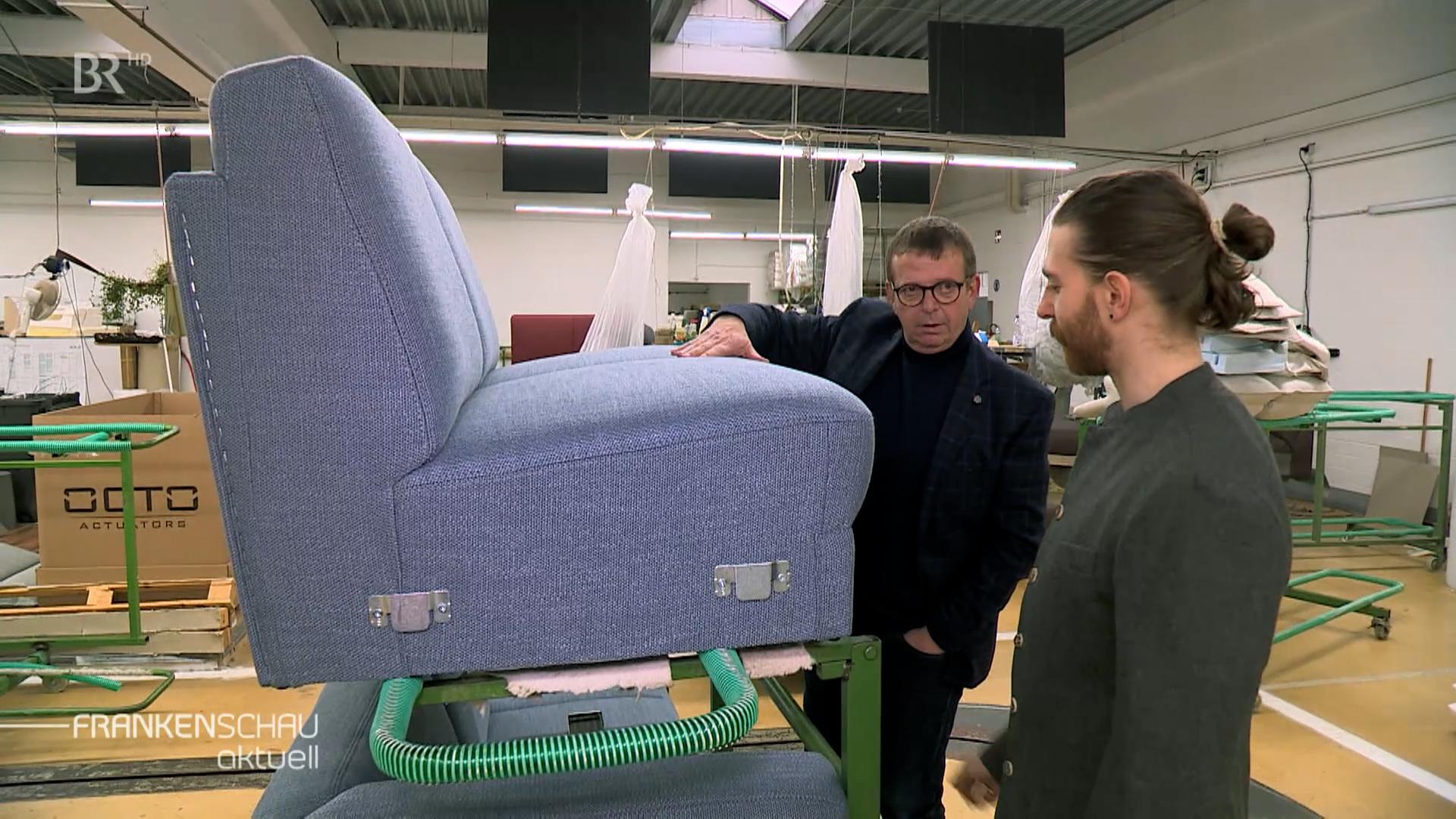 Zwei Männer betrachten eine blaues Polstermöbel und unterhalten sich.