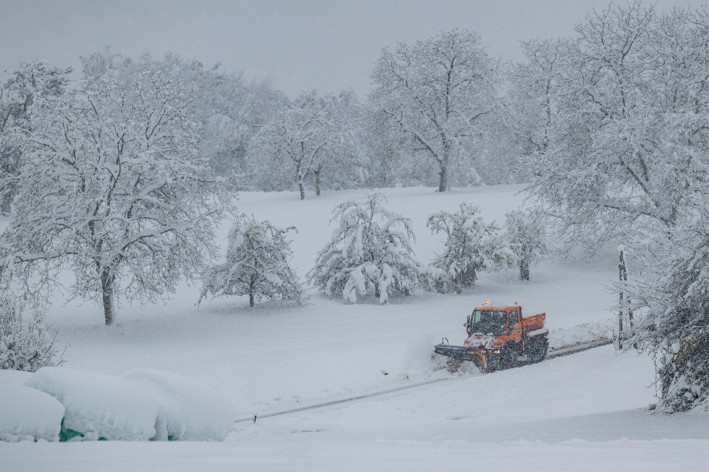 Ein Räumfahrzeug fährt durch die verschneite Landschaft (Windberg, Bayern)