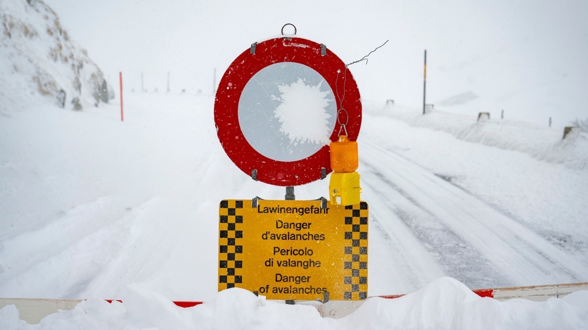 Ein Schild vor einer verschneiten Straße, das auf Lawinengefahr hinweist.