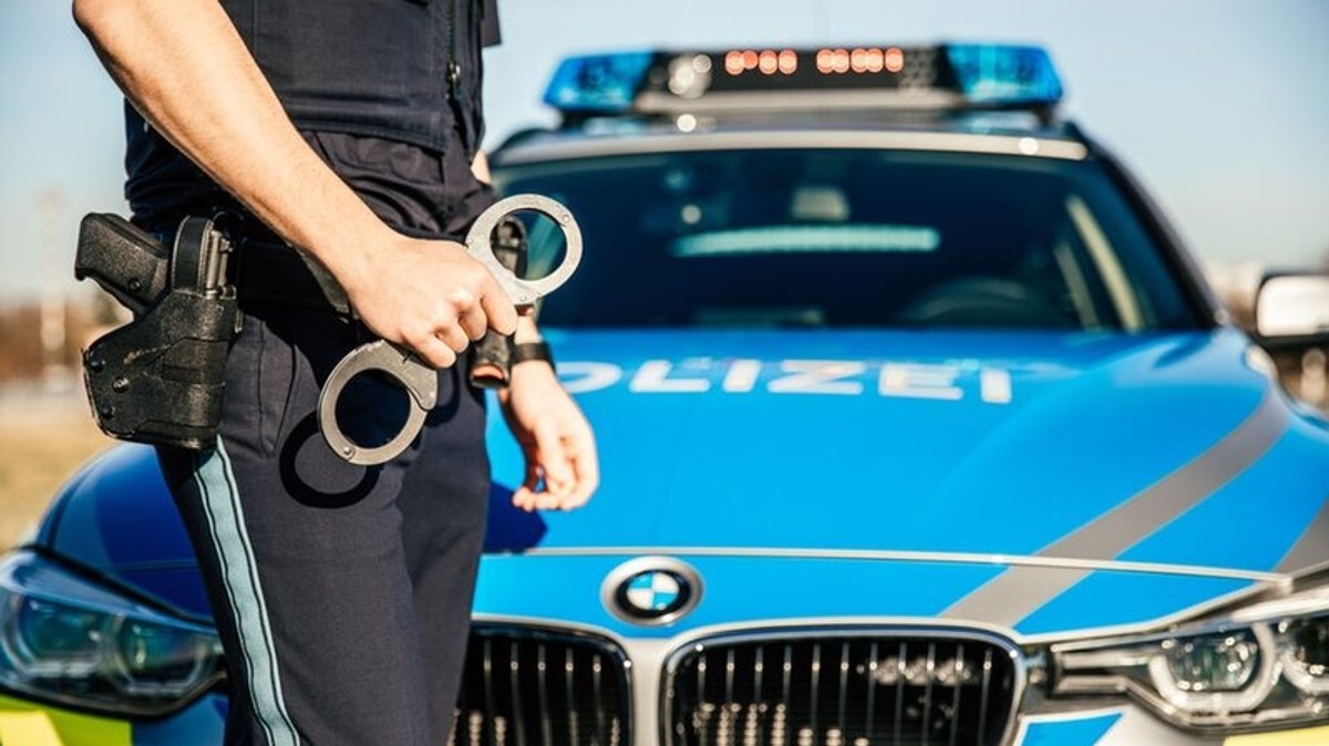 Polizist steht mit Handschellen vor einem Polizeiwagen 