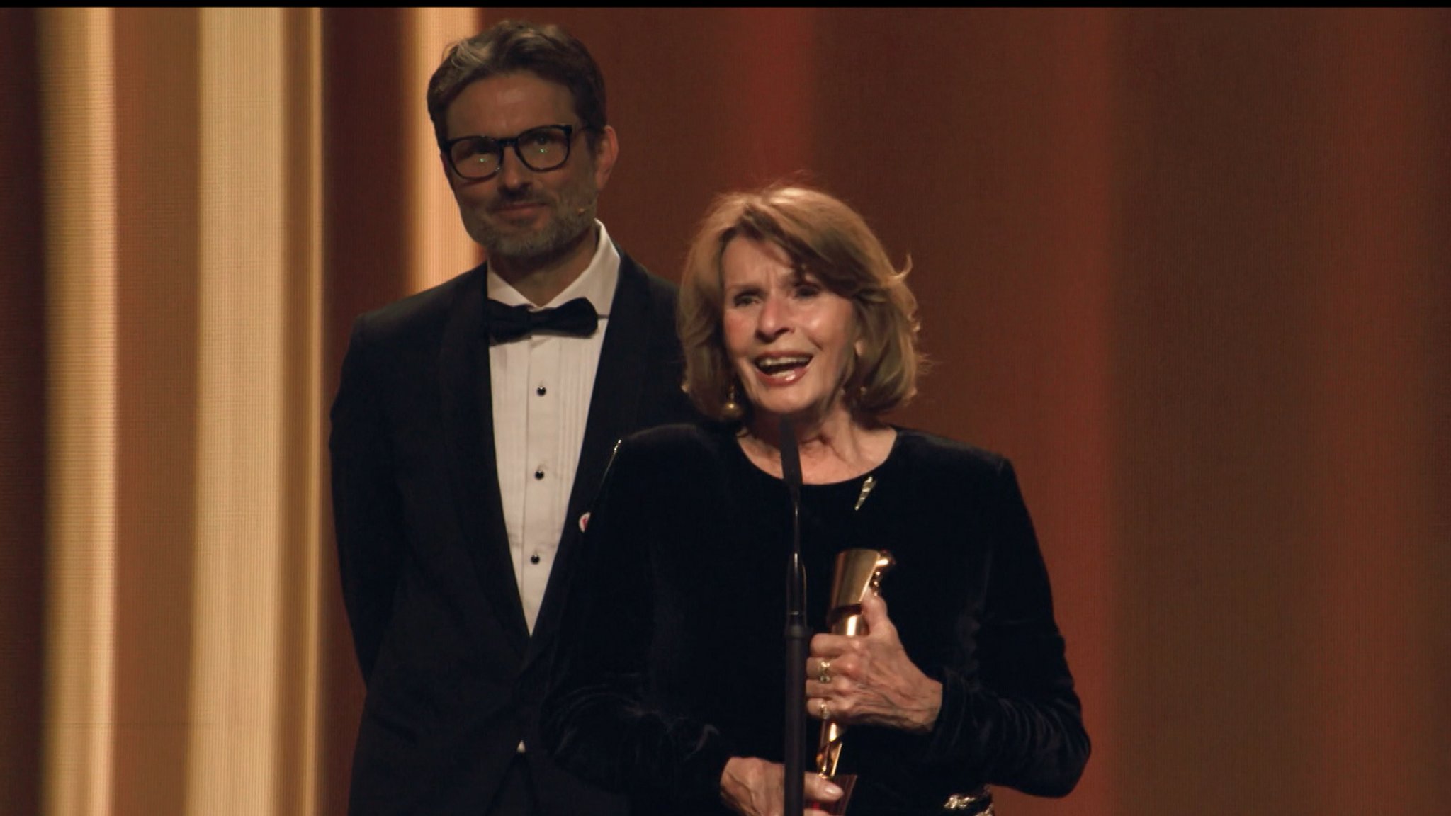 Senta Berger hält den Deutschen Filmpreis in ihren Händen; dahinter steht ihr Sohn, Regisseur Simon Verhoeven. | Bild: BR24 Senta Berger hält den Deutschen Filmpreis in ihren Händen; dahinter steht ihr Sohn, Regisseur Simon Verhoeven.