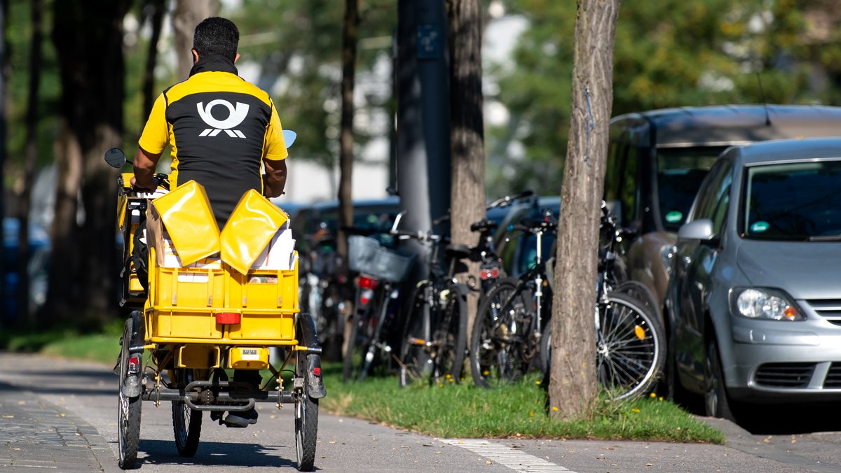 Ein Briefträger fährt mit seinem Fahrrad eine Straße in München entlang. 
