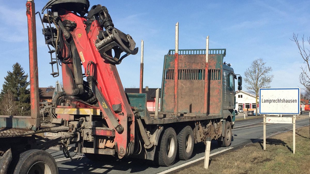 Ein unbeladener Holztransport-Lastwagen passiert das Ortsschild des österreichischen Orts Lamprechtshausen.