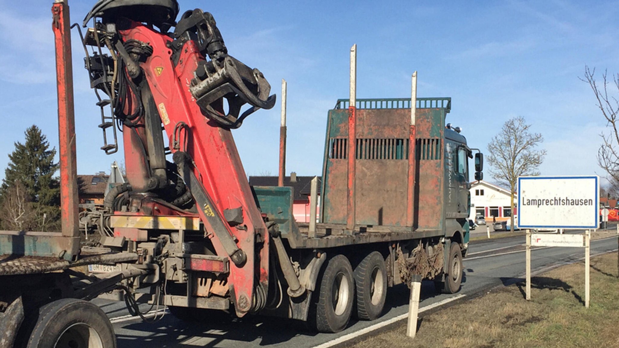 Ein unbeladener Holztransport-Lastwagen passiert das Ortsschild des österreichischen Orts Lamprechtshausen.