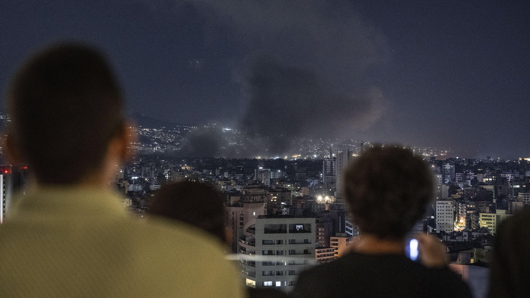 Menschen schauen in Beirut auf Rauchschwaden nach israelischen Angriffen.   