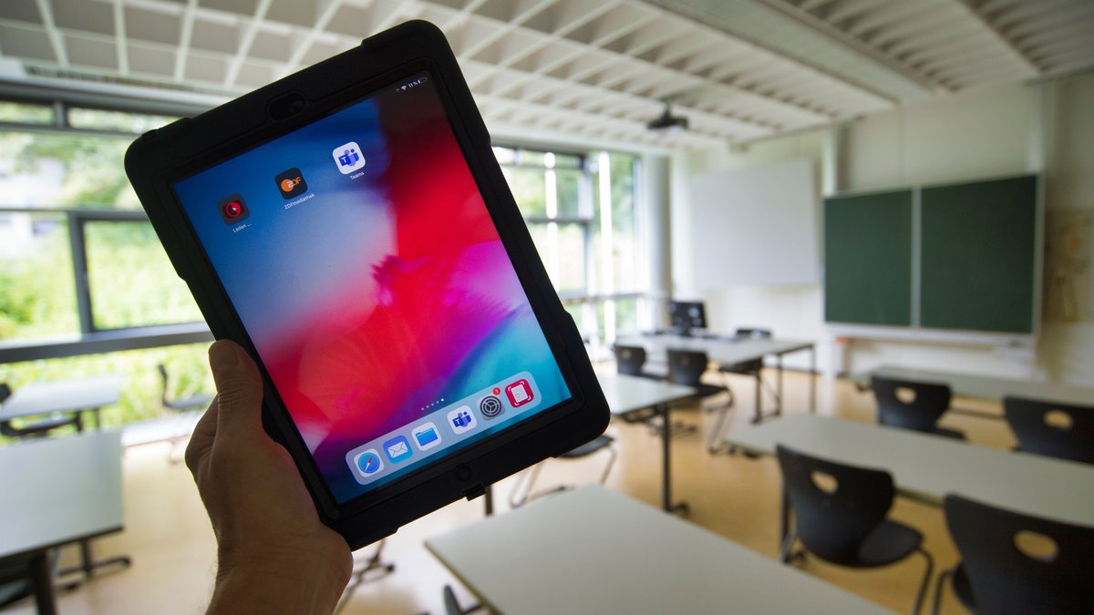 Hand hält Tablet in einem Klassenzimmer