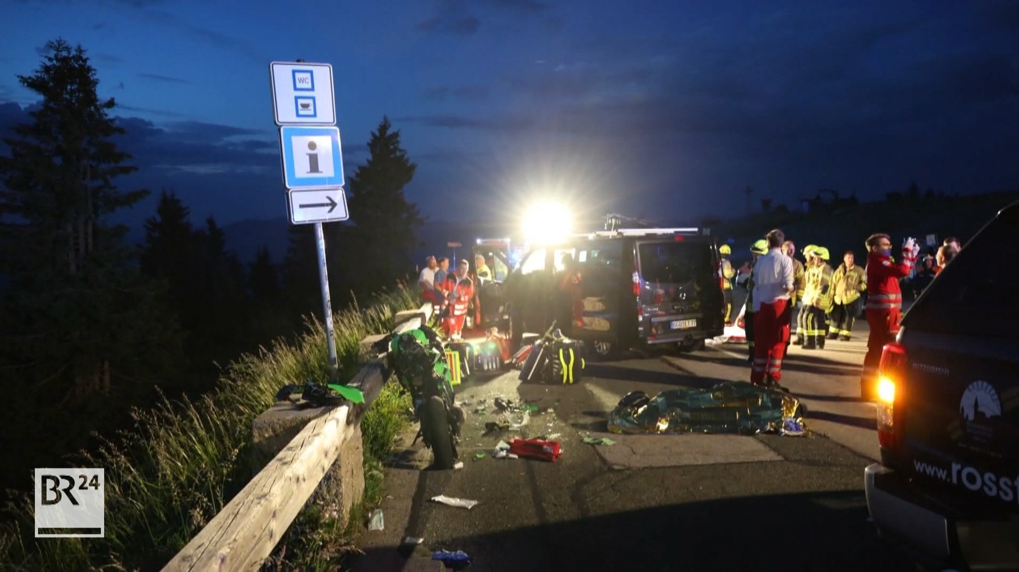 Die Unfallstelle eines Motorradunfalls in der Dunkelheit. Im Vordergrund links das zerstörte Motorrad, im Hintergrund viele Einsatz- und Rettungskräfte.