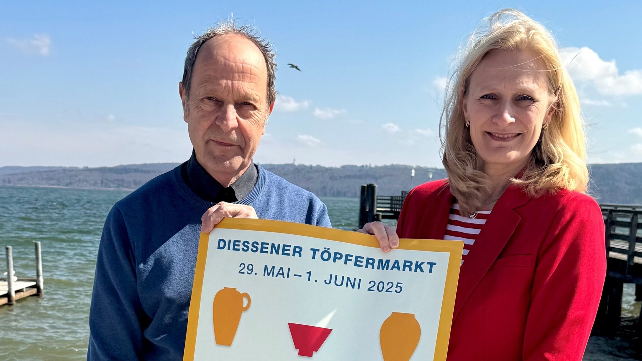 Dießens Erste Bürgermeistern Sandra Perzul und Marktleiter Wolfgang Lösche präsentieren das offizielle Werbeplakat am Ufer des Ammersees