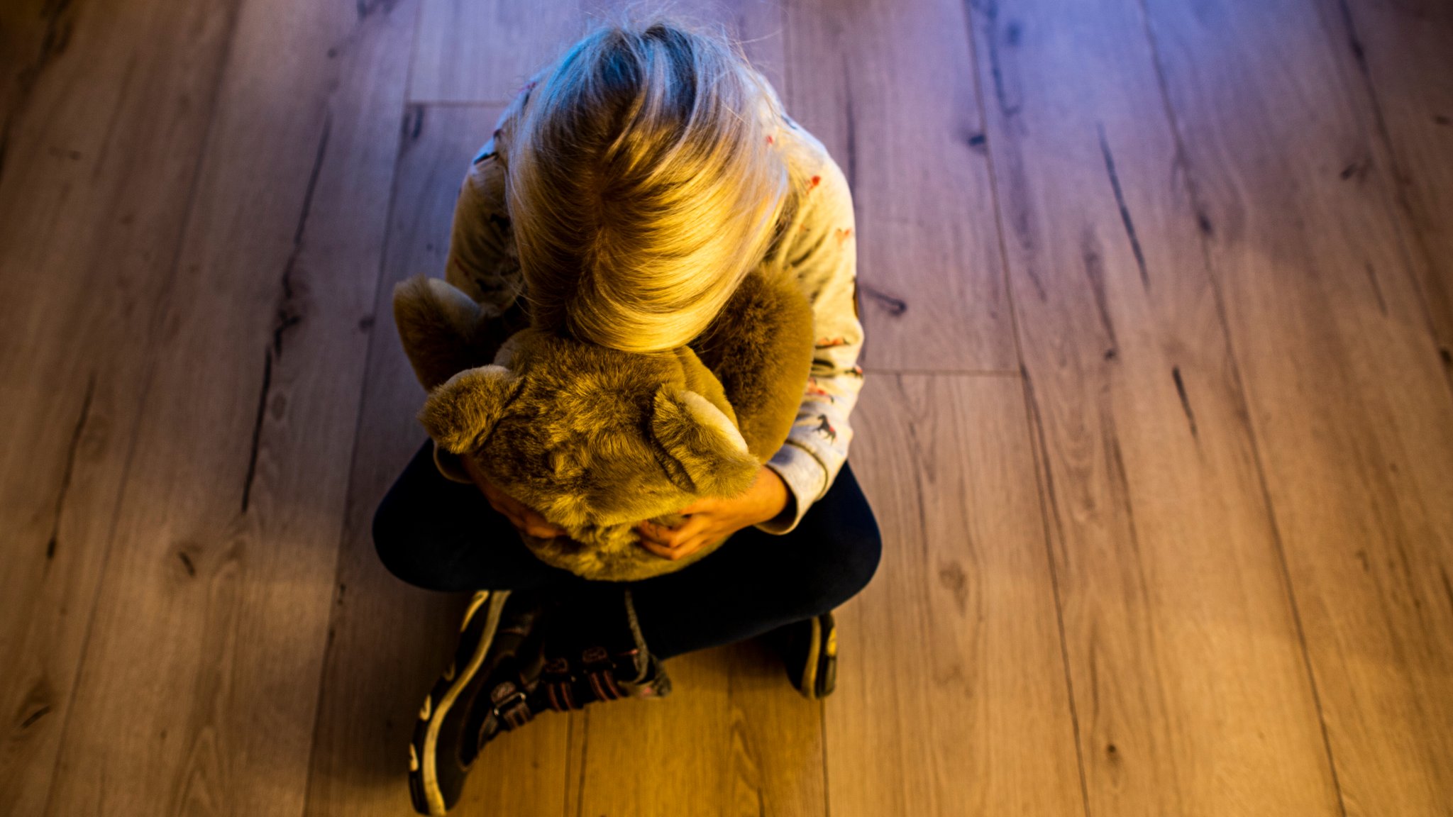 Ein Mädchen sitzt auf dem Boden und versteckt ihr Gesicht in einem Teddybär.