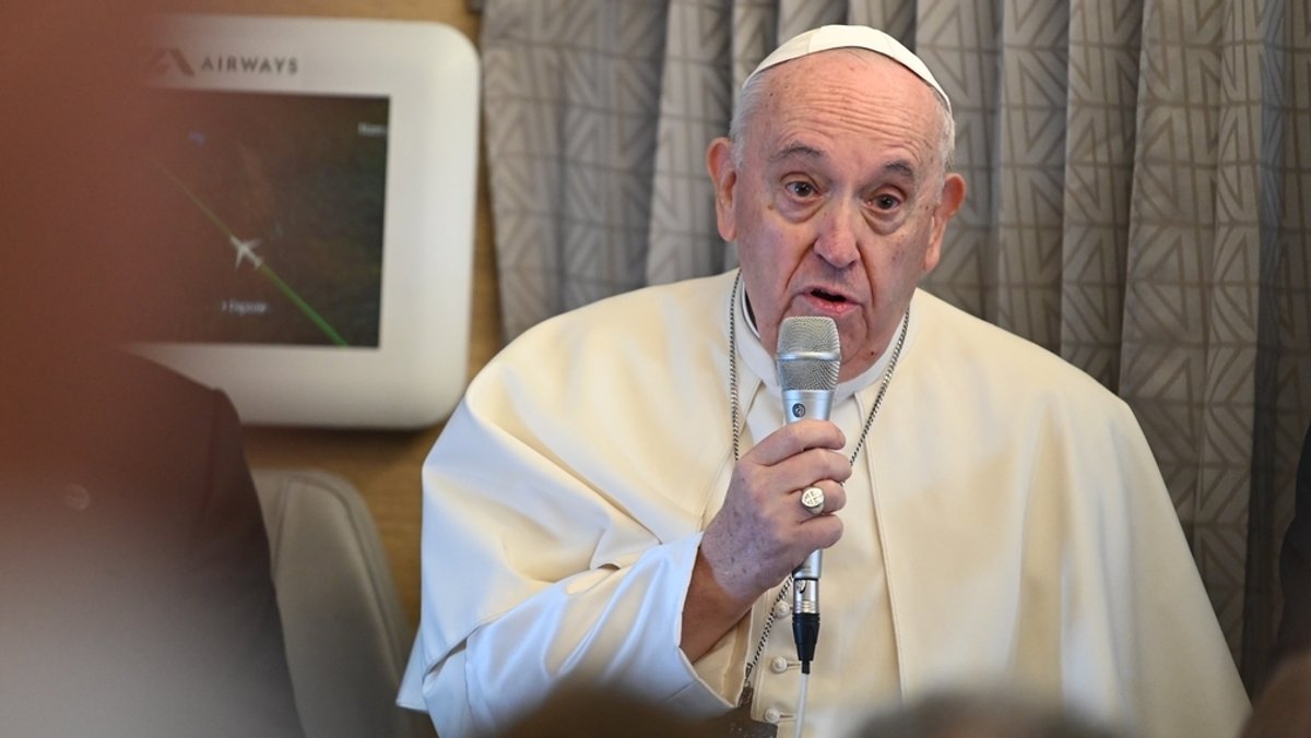 Papst Franziskus befindet sich in einem Flugzeug und hat ein Mikrophon in der Hand. Er spricht zu Journalisten auf dem Flug nach Kanada.