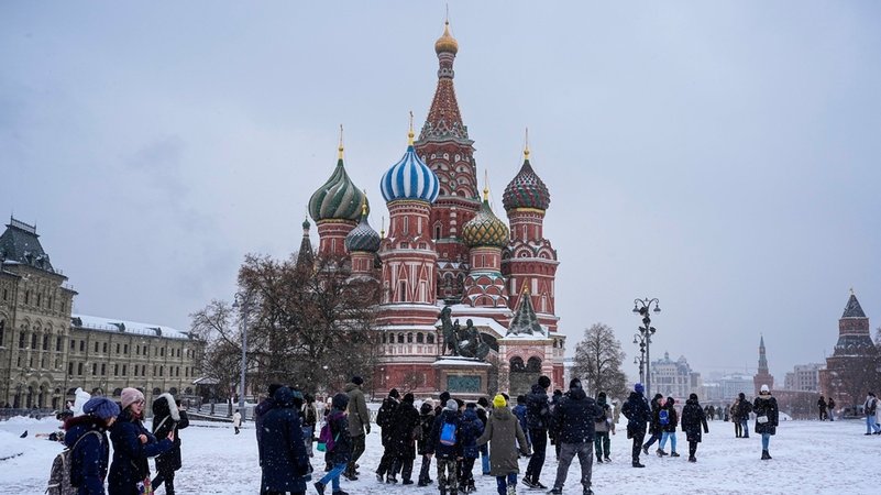 Russland, Moskau: Menschen gehen über den schneebedeckten Roten Platz, während die Basilius-Kathedrale im Hintergund zu sehen ist.
