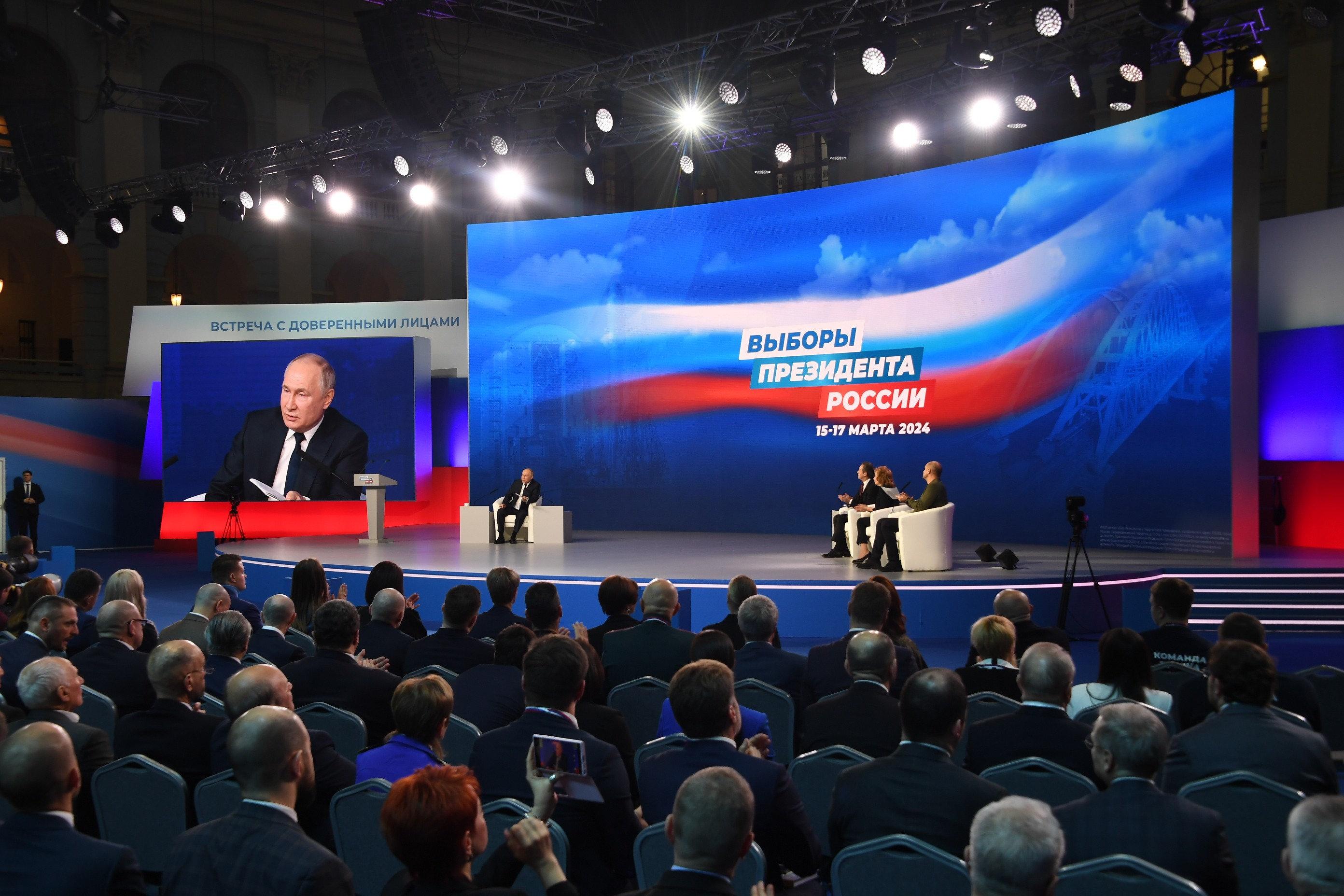 Der Präsident auf einer Bühne sitzend vor Werbebanner