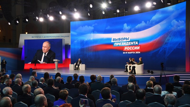 Der Präsident auf einer Bühne sitzend vor Werbebanner | Bild: Komsomolskaya Pravda/Picture Alliance Der Präsident auf einer Bühne sitzend vor Werbebanner