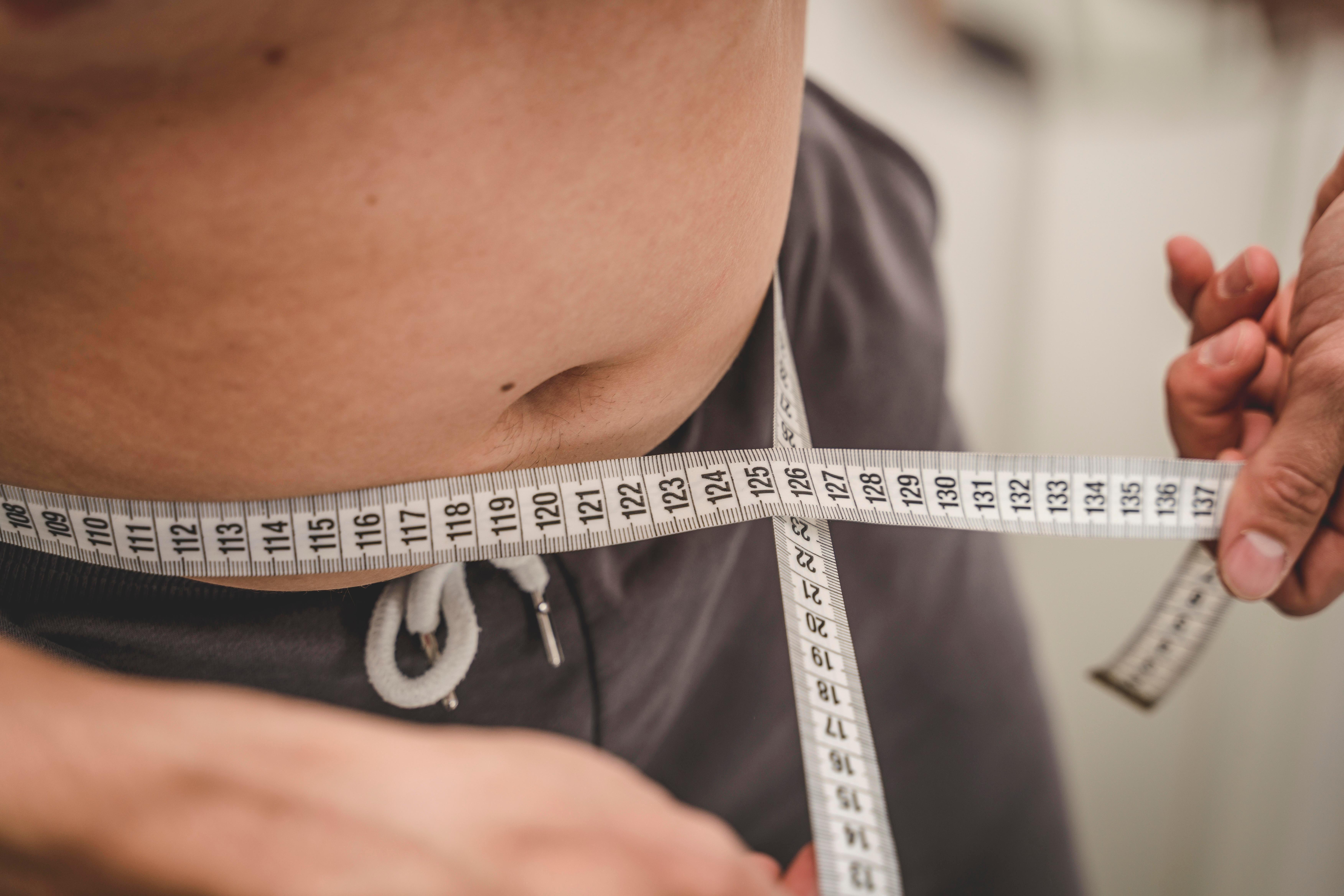 Junger Mann misst mit einem Maßband den Umfang seines Bauchs (Symbolbild)