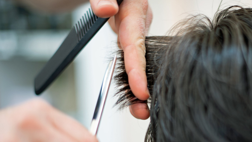 Ein Friseur schneidet in einem Friseur-Salon einer Kundin mit einer Schere die Haare.