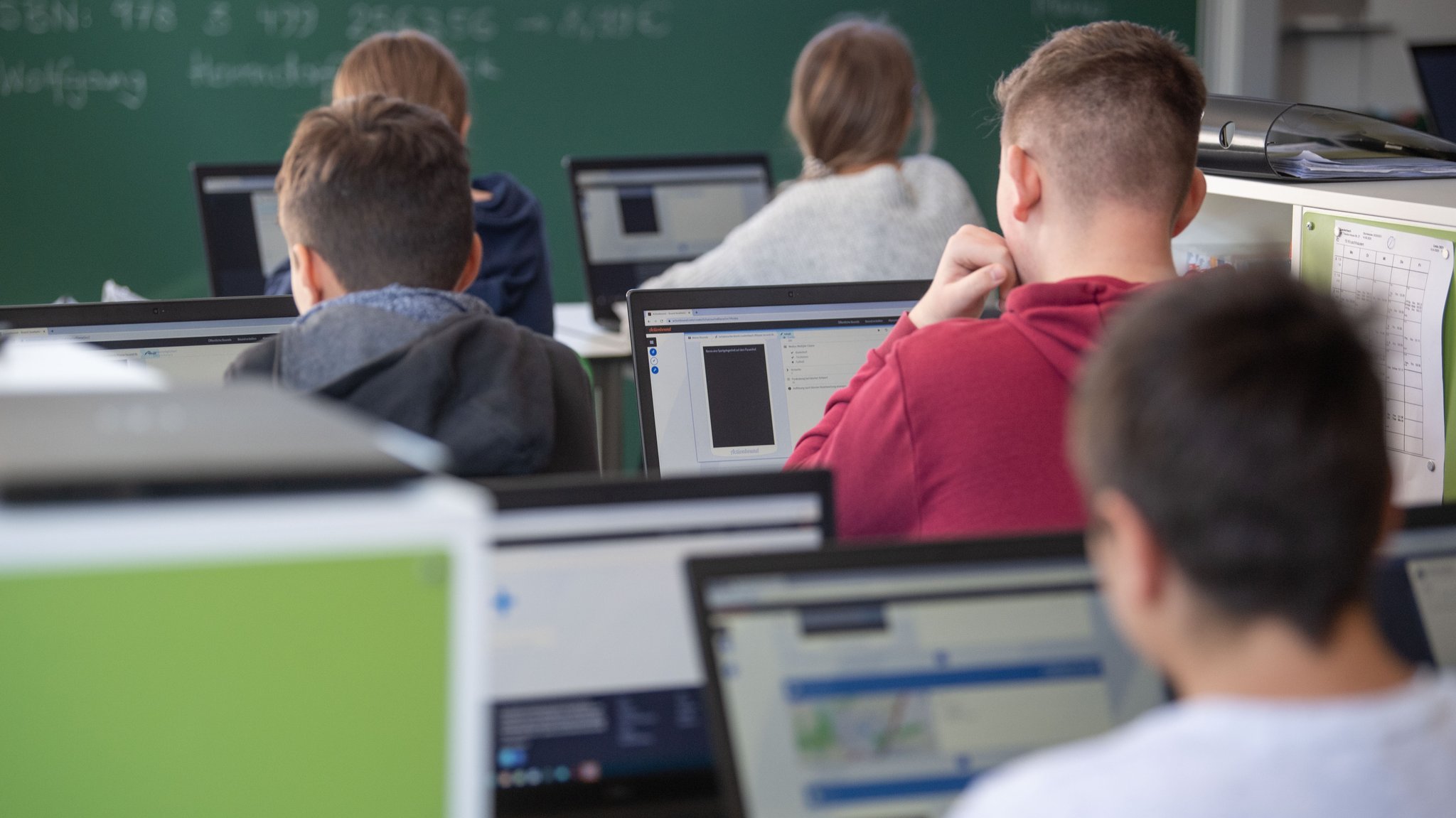 Schülerinnen und Schüler im Klassenzimmer einer 9. Klasse nehmen am Geografieunterricht mit Hilfe von Laptops und Tablets teil.