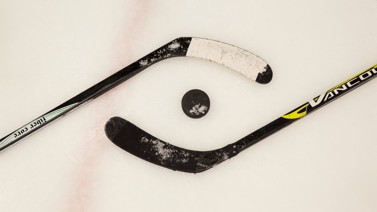 Zwei Eishockeyschläger liegen auf dem Eis, in der Mitte liegt ein Puck (Symbolbild).