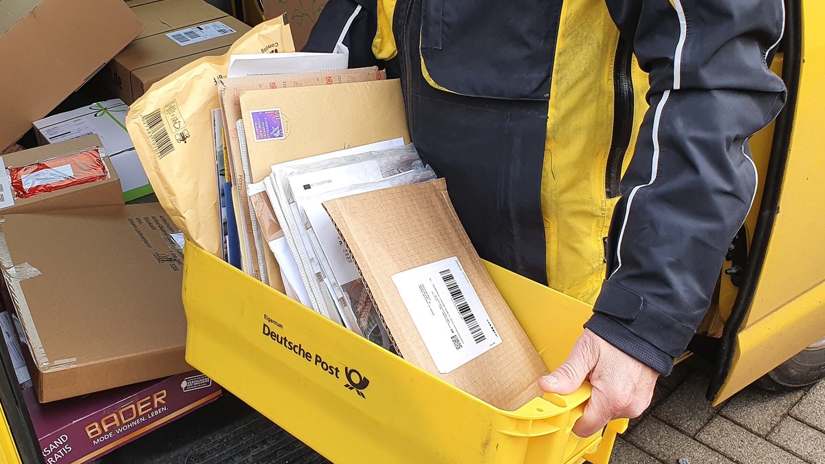 Ein Briefträger mit einem Kasten voller Briefe und Päckchen.