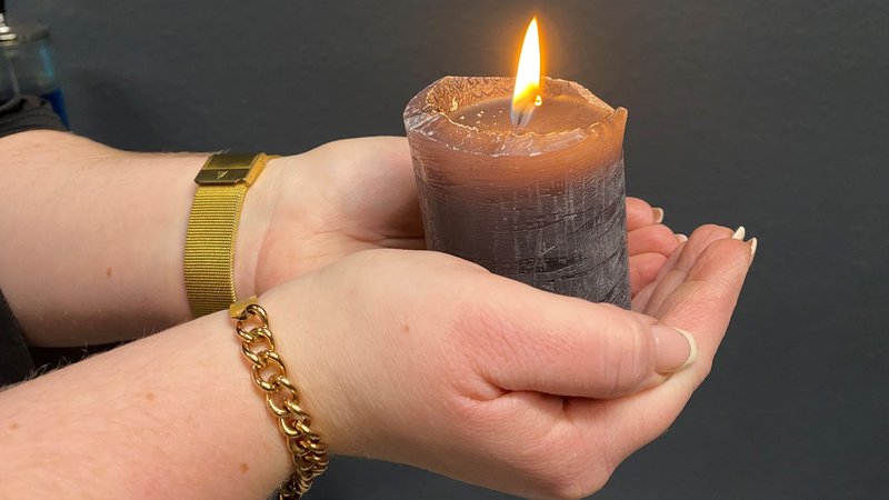 Zwei Hände halten eine brennende Kerze. 