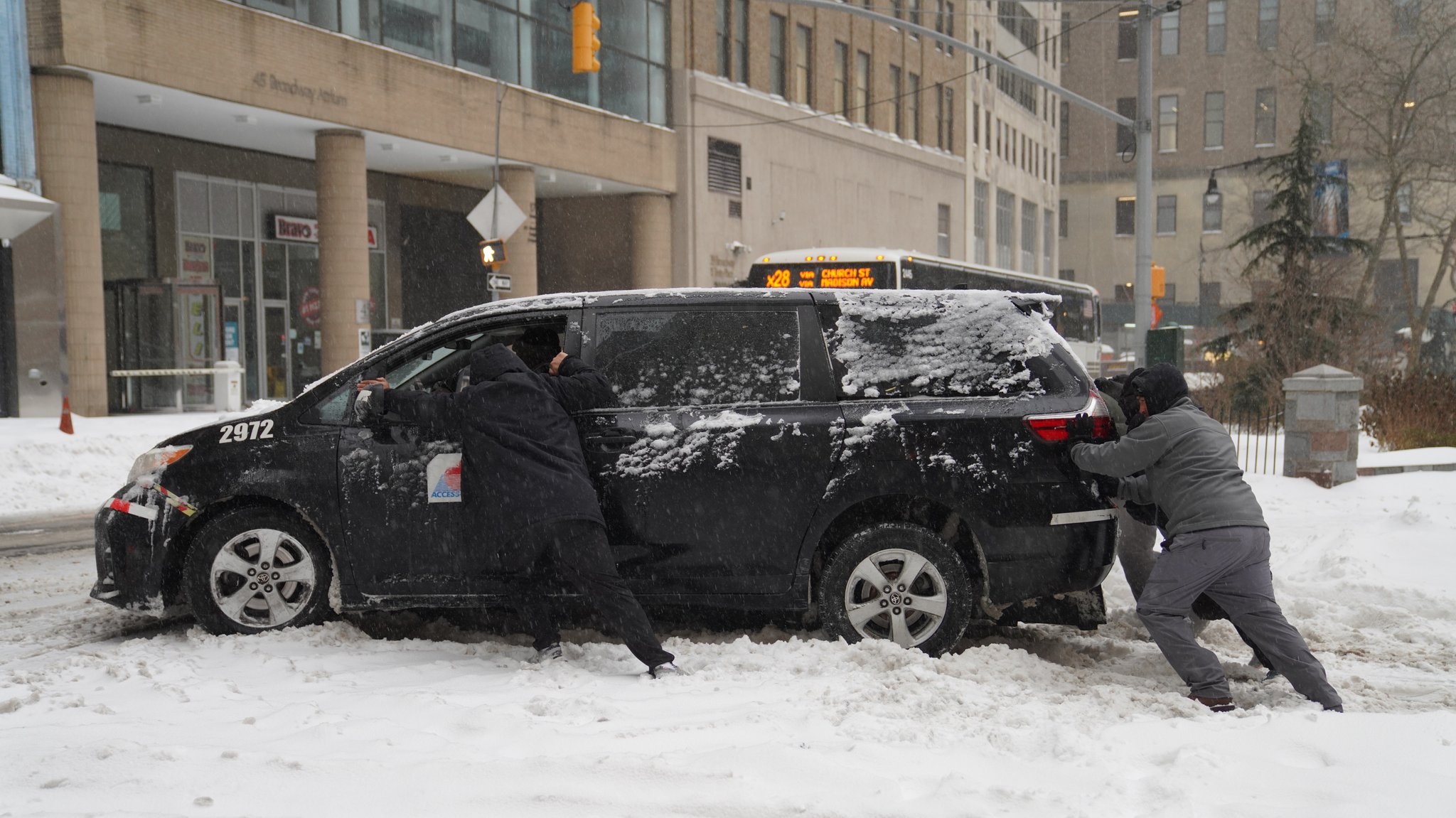 Menschen schieben in New York ein im Schnee festgefahrenes Auto.