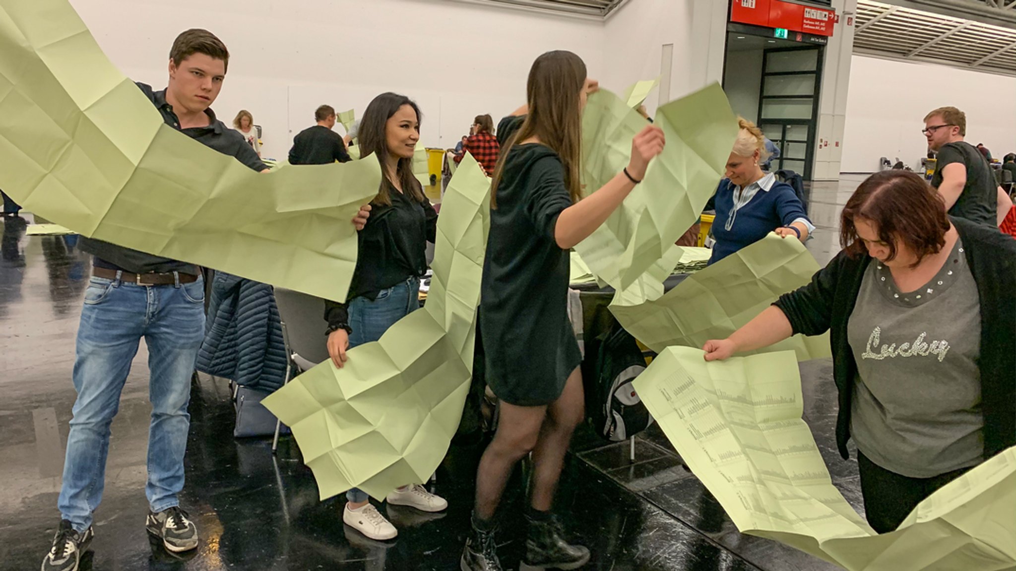 Viele Wahlhelferinnen und Helfer halten die riesigen grünen Stimmzettel für den Münchner Stadtrat in Händen - er ist 1,5 Meter lang. | Bild: BR/Sabine Konvalin Viele Wahlhelferinnen und Helfer halten die riesigen grünen Stimmzettel für den Münchner Stadtrat in Händen - er ist 1,5 Meter lang.