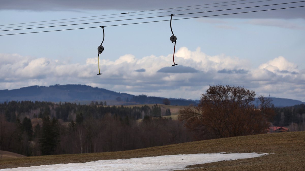 Teller eines Schleppliftes hängen über einem Kunstschneestreifen in der schneelosen Landschaft. 
