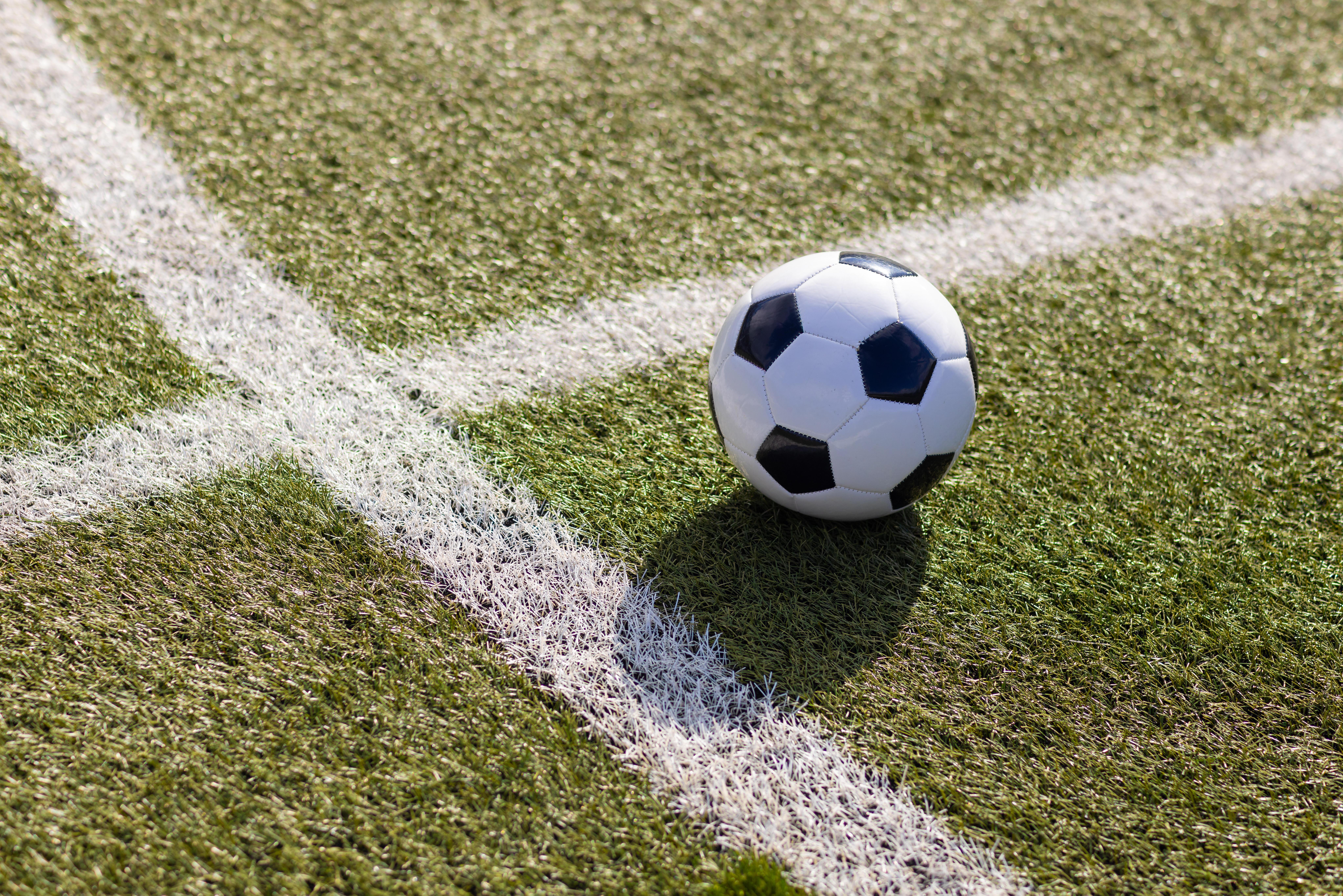 (Symbolbild) Klassischer Fußball liegt bei Sonnenschein auf trockenem Fußballrasen.
