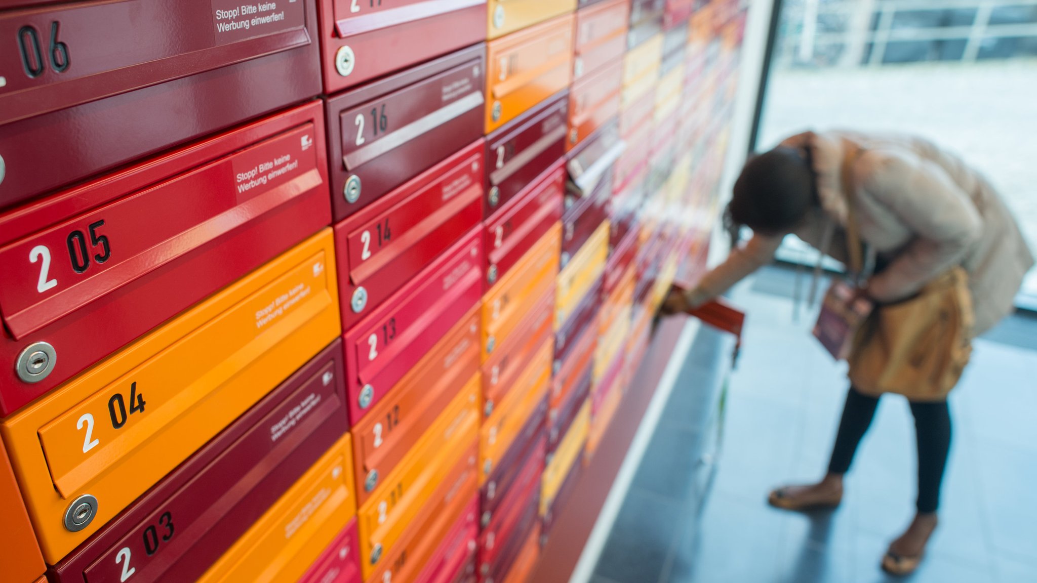 Bunte Briefkästen in rot und orange, im Hintergrund holt eine Studentin ihre Post aus dem Fach. 