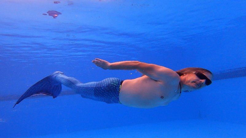 Ingenieur Alexander Sengpiel schwimmt als Atlan, der Meerjungmann, mit Monoflosse und langen Haaren unter Wasser in einem Pool