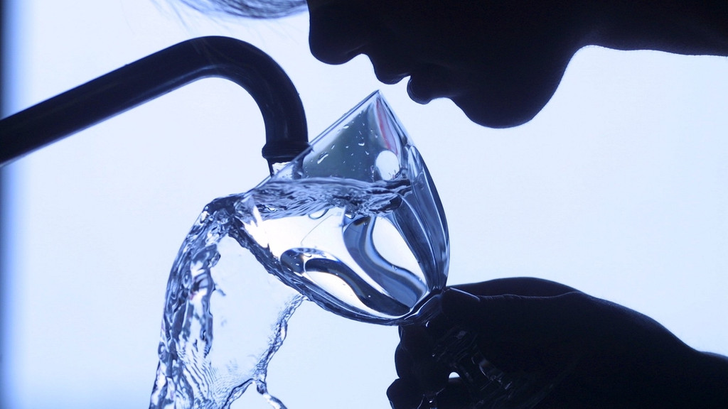 eine Frau füllt ein Wasserglas unter dem Wasserhahn