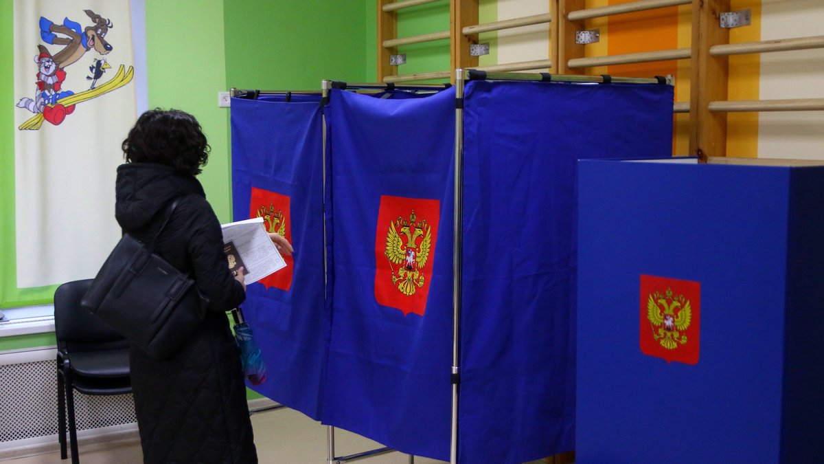 Eine Frau steht vor einer Wahlkabine in Russland.