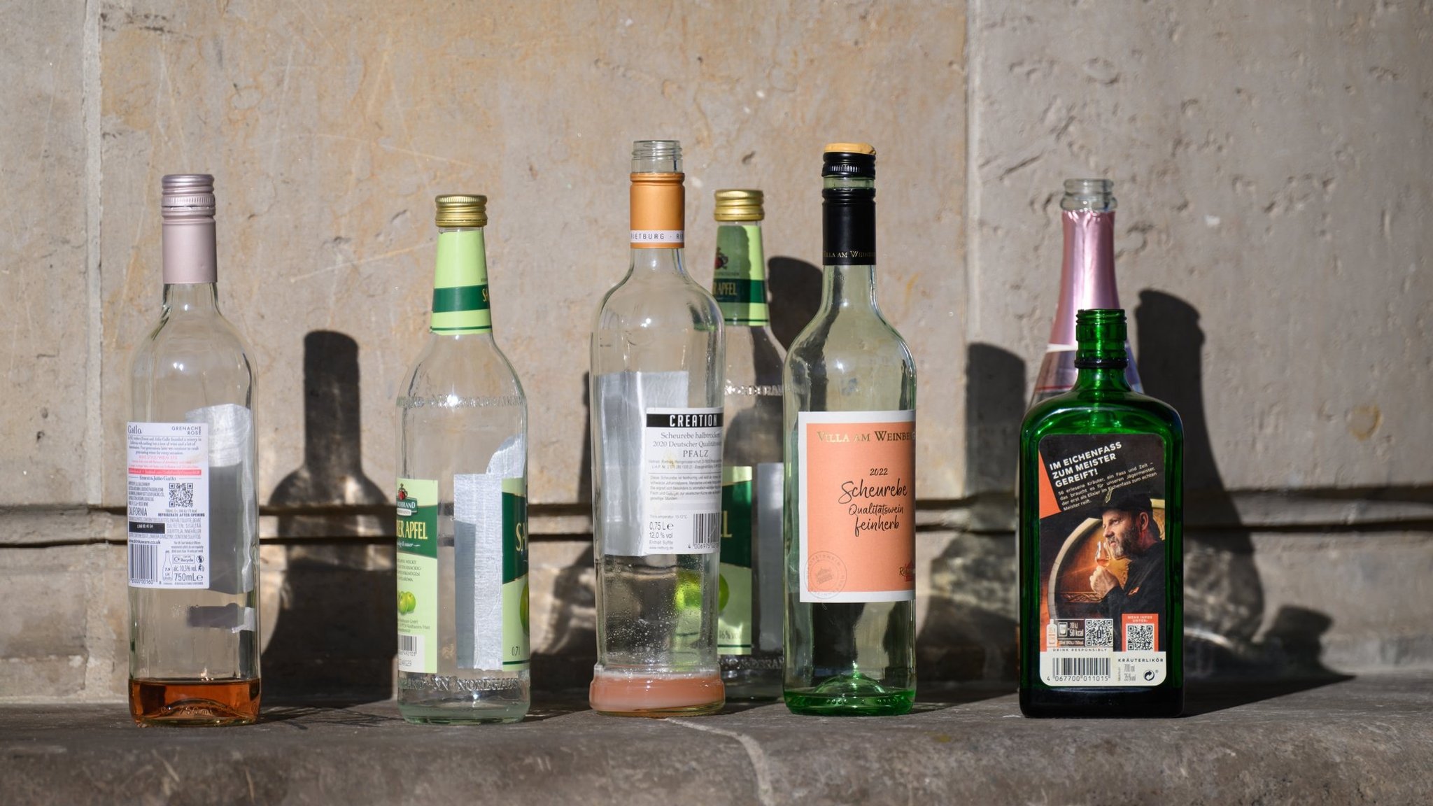 Leere oder fast leere Flaschen mit alkoholischem Inhalt stehen auf einer Mauer.