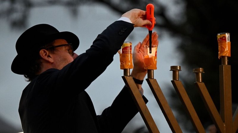Ein Rabbi entzündet eine Menora während einer Mahnwache in Bondi Beach. Australien trauert, nachdem zwei bewaffnete Männer am Bondi Beach eine jüdische Feier angriffen und 16 Menschen töteten. | Bild: dpa-Bildfunk/Bianca De Marchi Ein Rabbi entzündet eine Menora während einer Mahnwache in Bondi Beach. Australien trauert, nachdem zwei bewaffnete Männer am Bondi Beach eine jüdische Feier angriffen und 16 Menschen töteten.