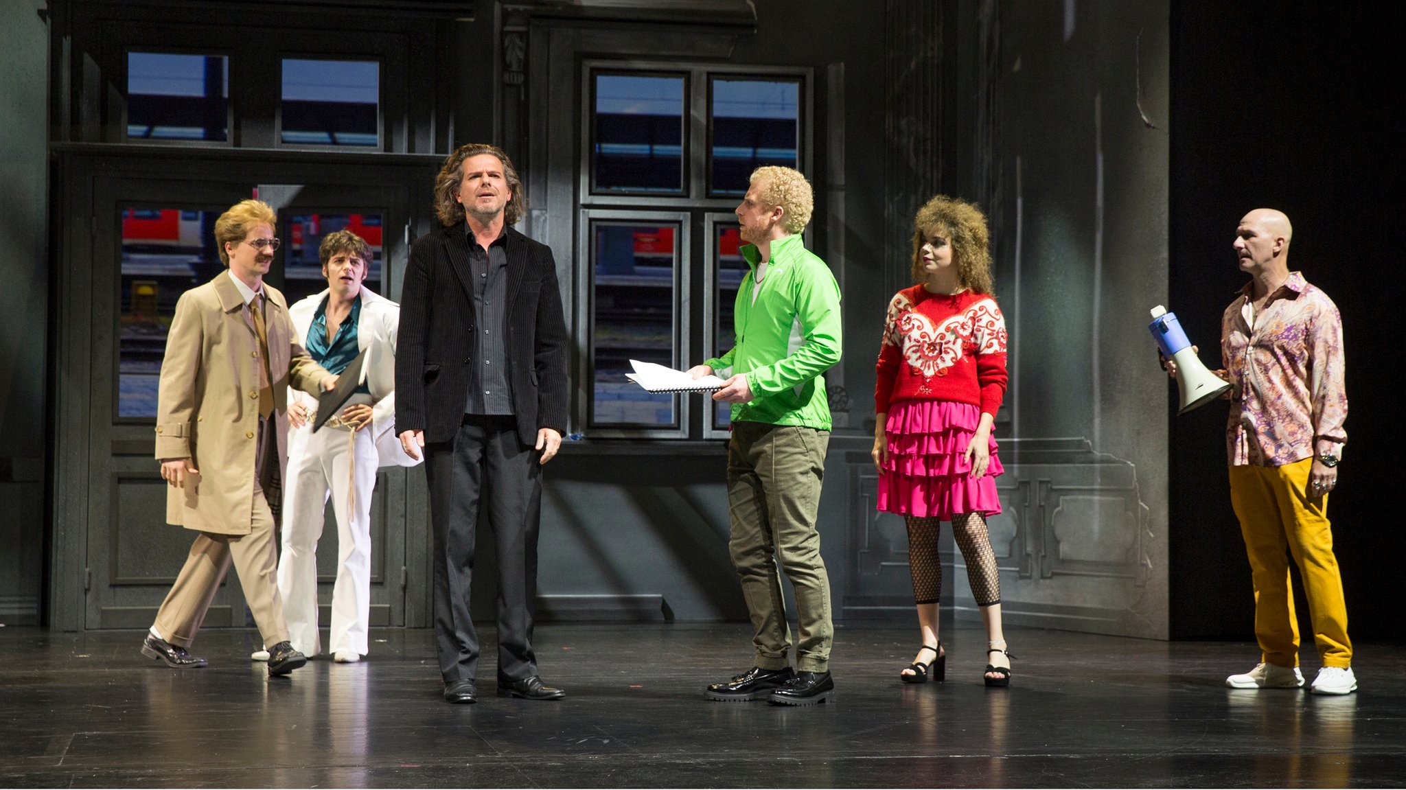 Sechs Schauspieler stehen auf der Bühne im Hofer Theater. Die Kulisse zeigt den Hofer Hauptbahnhof. 